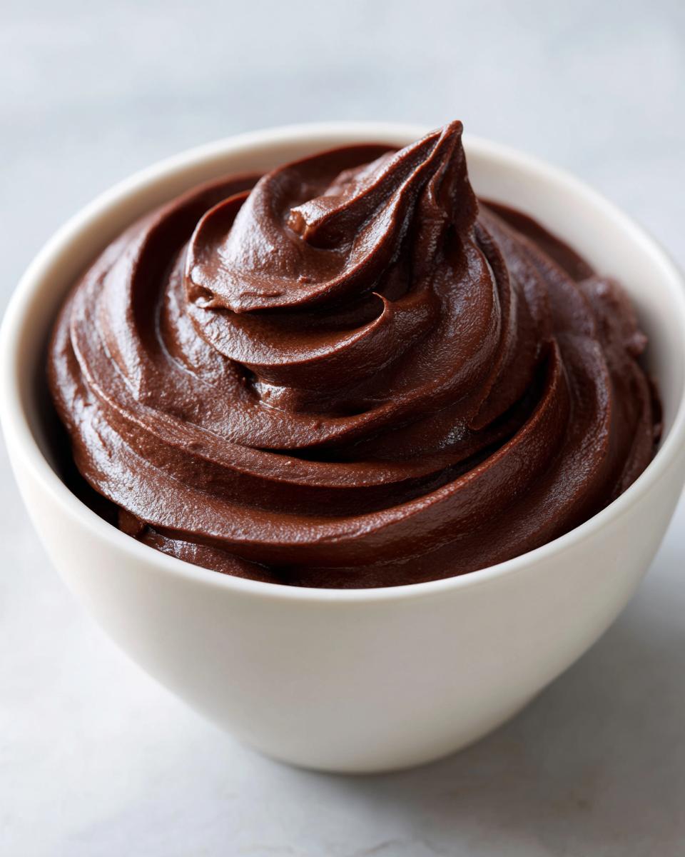 A close-up of rich chocolate frosting recipe swirled in a white bowl.
