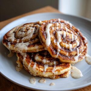 A stack of fluffy cinnamon roll pancakes drizzled with a creamy white glaze.