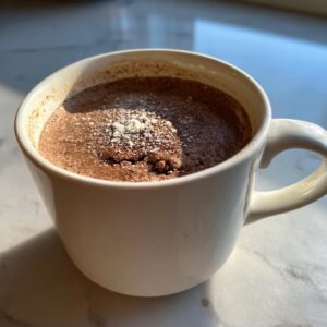 A close-up of a warm Cottage Cheese Microwave Brownie in a white mug, dusted with powdered sugar.