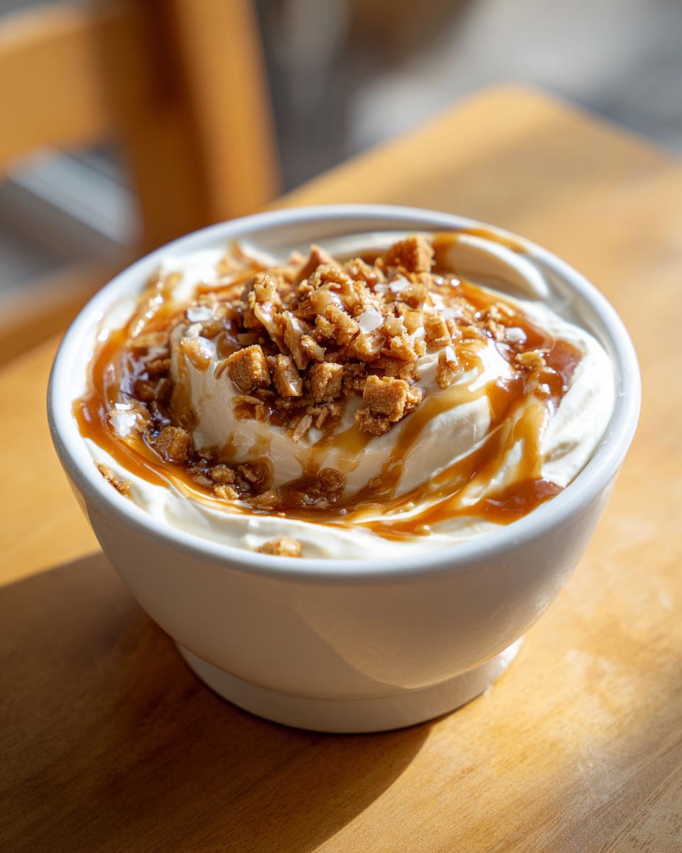 A close-up of a white bowl filled with creamy cream cheese caramel dip, drizzled with caramel sauce and topped with crushed cookies.