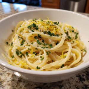 A close-up of a bowl of creamy lemon pasta, garnished with fresh parsley and lemon zest.