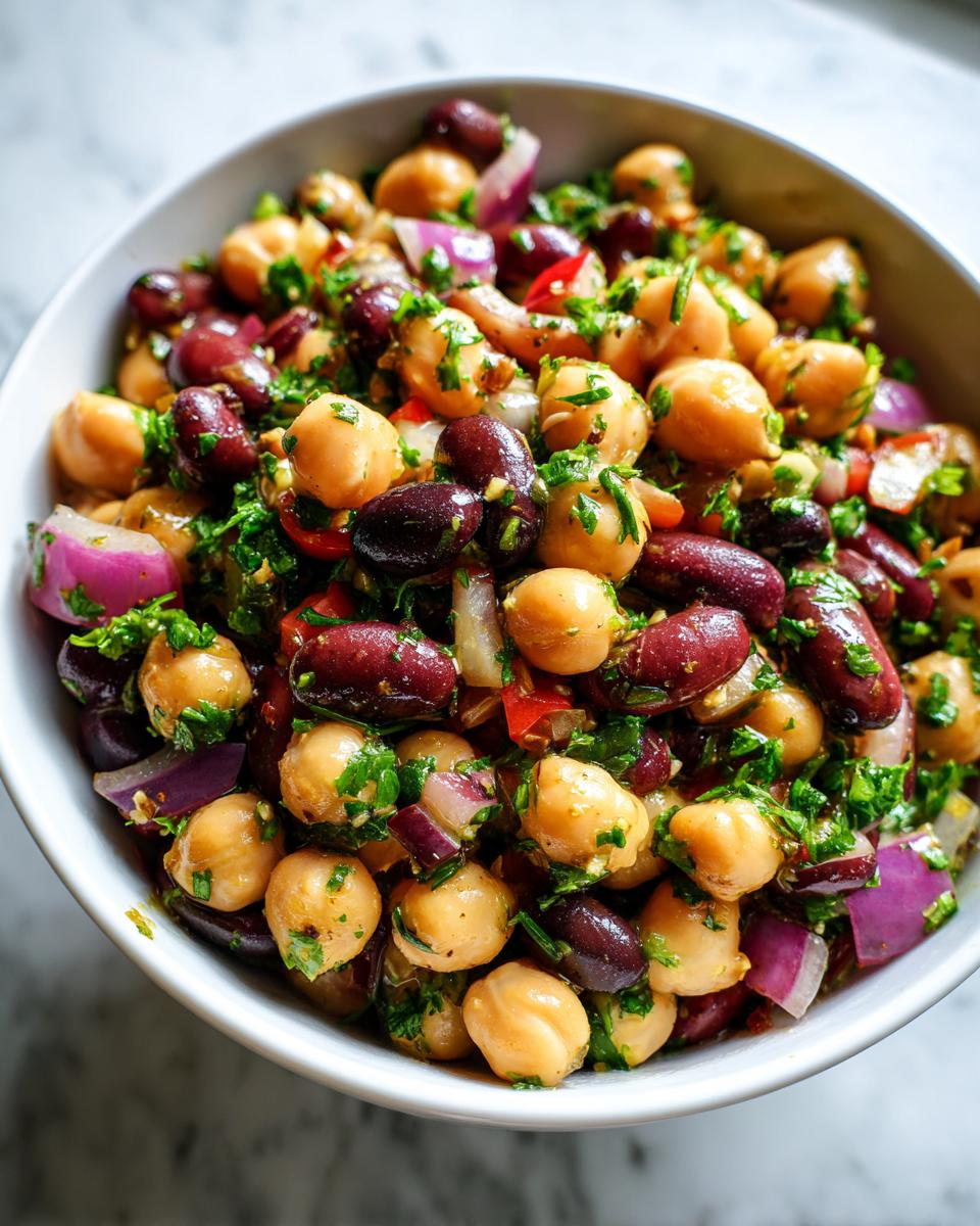 Close-up of a vibrant Dense Bean Salad featuring chickpeas, kidney beans, red onion, and fresh parsley.