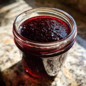 Close-up of a glass jar filled with rich, dark purple Elderberry Syrup.