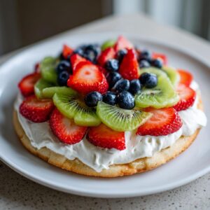 A vibrant fruit pizza sugar cookie topped with whipped cream, strawberries, kiwi slices, and blueberries.