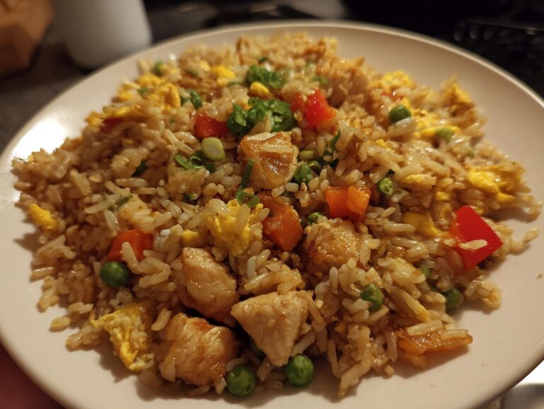 A close-up of a plate filled with high protein garlic chicken fried rice, featuring chunks of chicken, scrambled eggs, peas, carrots, and red bell peppers.