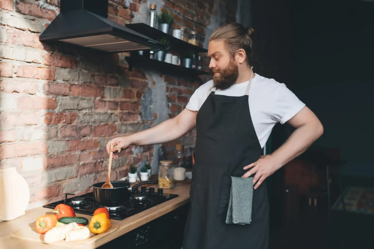 Leo Maxwell, founder of Gourmet Gaze, with a focused expression as he stirs a sauce in a pot on his stove, with a rustic brick wall in the background.