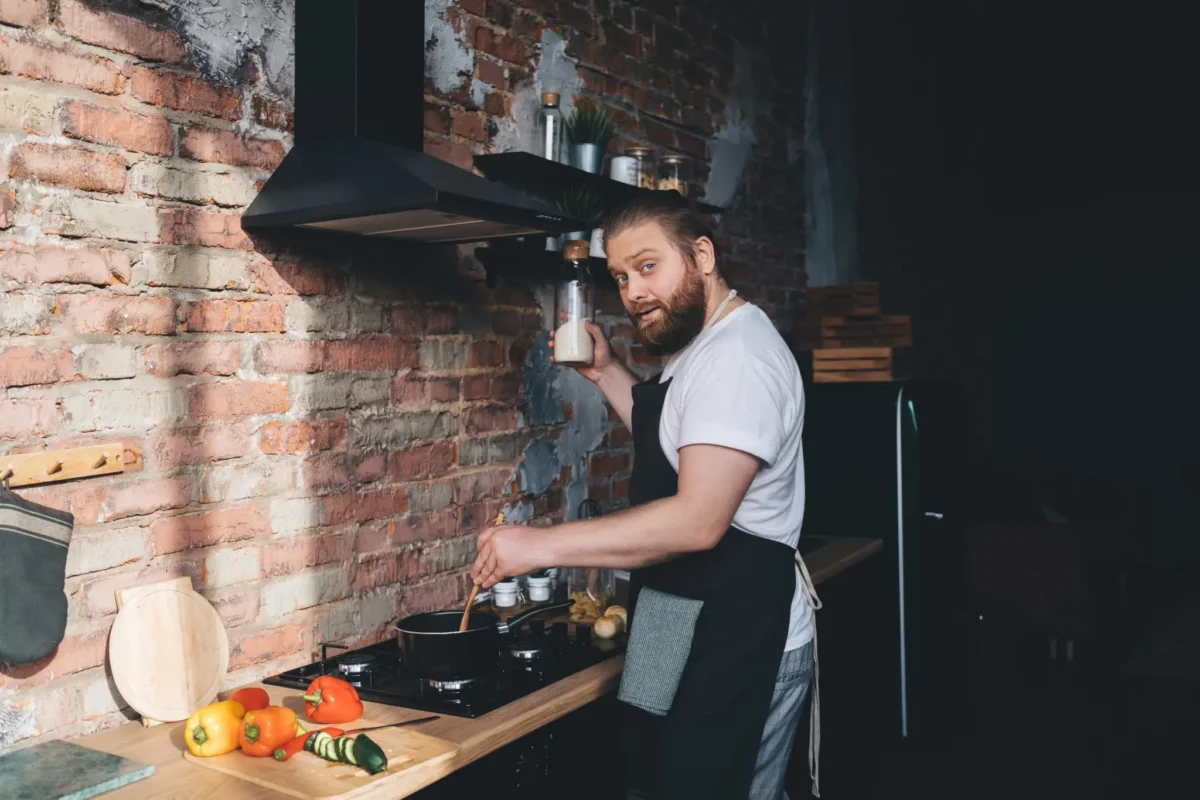 Chef Leo Maxwell of Gourmet Gaze smiling at the camera as he adds a pinch of salt to a dish he is cooking on the stovetop.