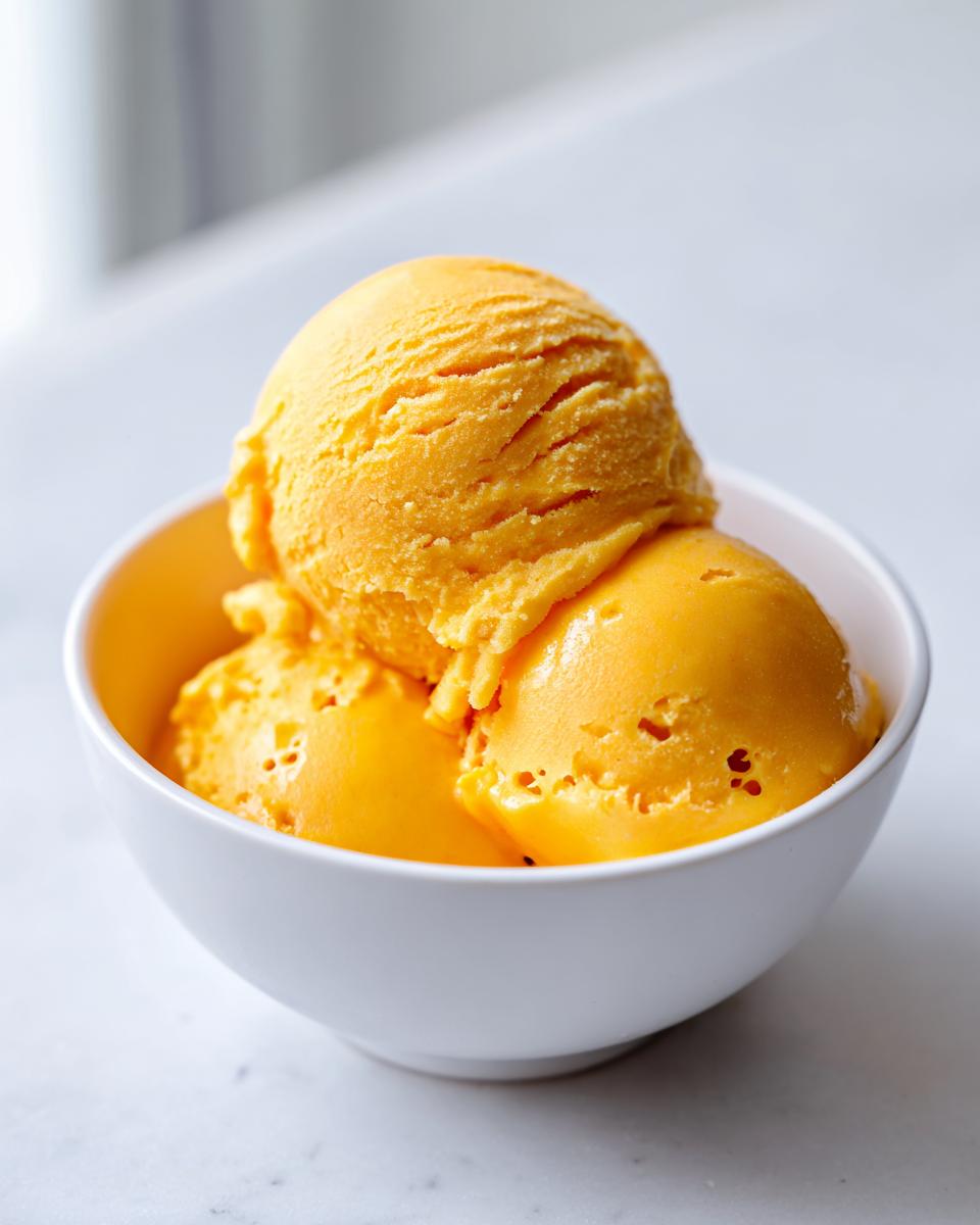 Three scoops of vibrant orange mango sorbet in a white bowl, perfect for beating the heat.