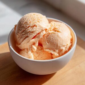 Close-up of three scoops of creamy papaya protein ice cream in a white bowl.