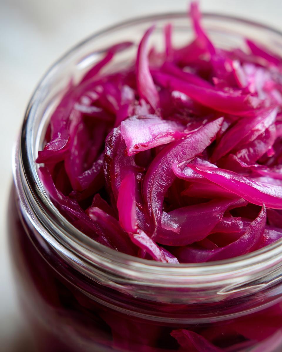 Close-up shot of a glass jar filled with bright pink pickled red onions.