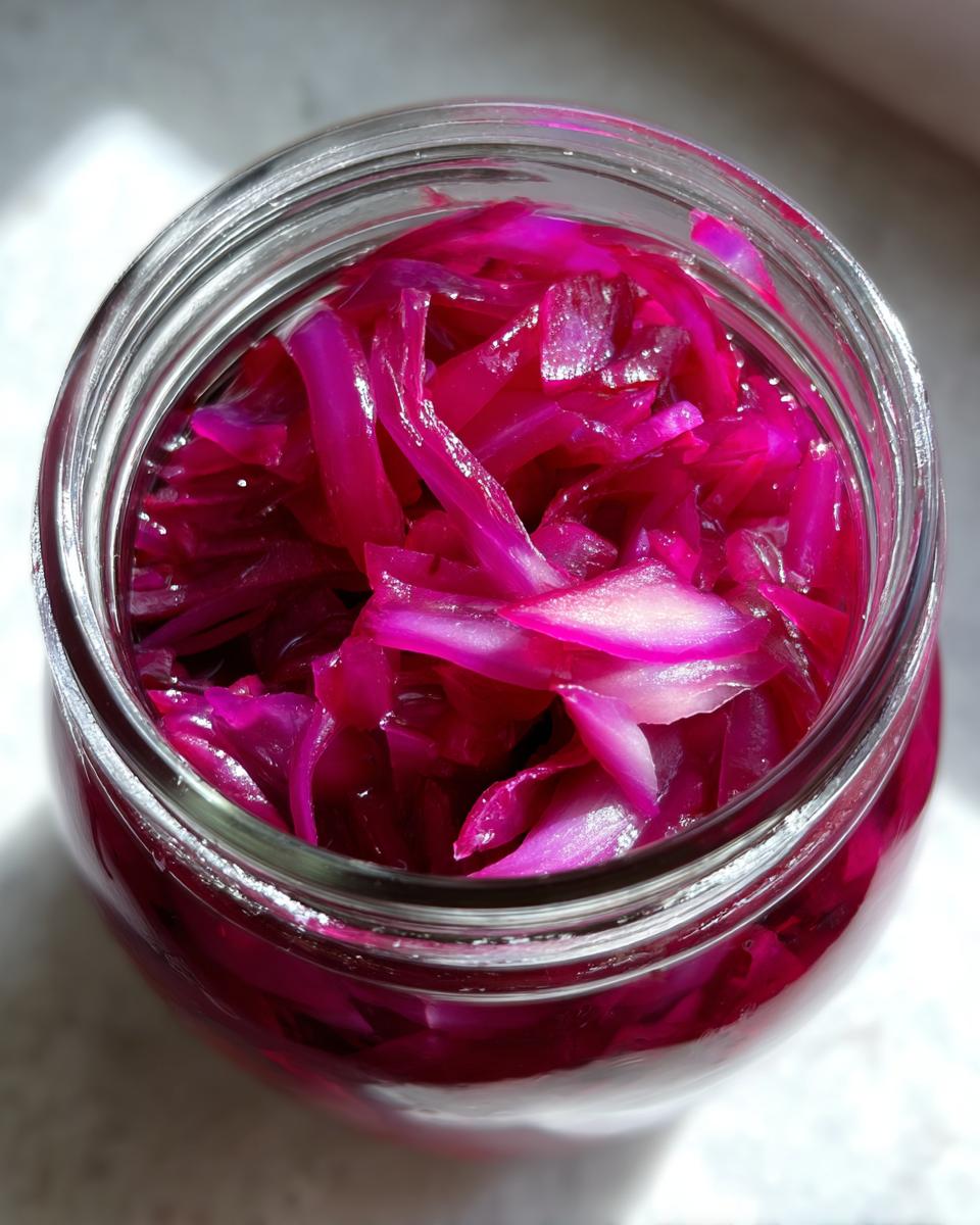 Close-up overhead view of a glass jar filled with vibrant pickled red onions.