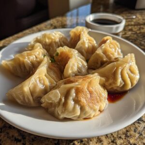 A plate of golden-brown pan-fried Traditional Chinese Dumplings served with soy sauce.