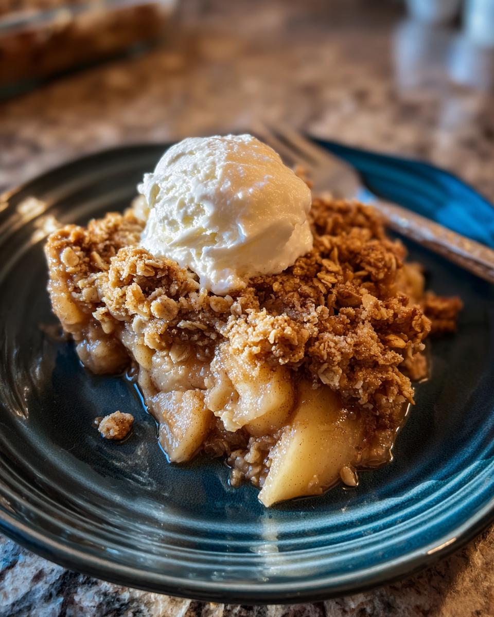 A warm slice of apple crisp topped with a scoop of vanilla ice cream on a blue plate.