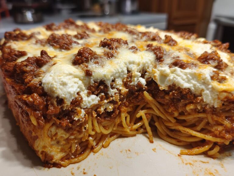 A close-up of a baked cream cheese spaghetti casserole, showing layers of spaghetti, meat sauce, and melted cheese.