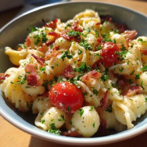 A close-up of a bowl of BLT pasta salad, featuring pasta shells, cherry tomatoes, crumbled bacon, and fresh parsley.