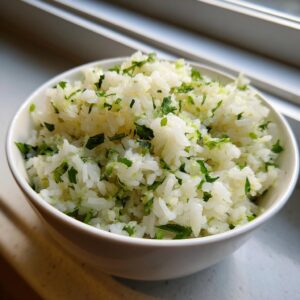 A close-up of a white bowl filled with fluffy cilantro lime rice, garnished with fresh green cilantro.