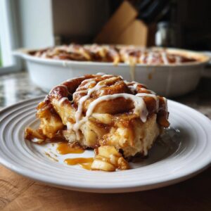 A close-up of a slice of cinnamon roll apple bake, drizzled with icing and caramel.