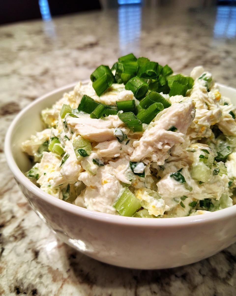 A close-up of a bowl filled with creamy classic chicken salad, topped with chopped green scallions.