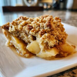 A close-up of a slice of warm apple crisp on a white plate, showing tender baked apples and a crumbly oat topping.