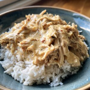 A bowl of fluffy white rice topped with shredded creamy ranch chicken crockpot in a rich sauce.