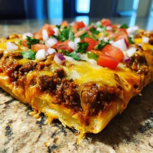 A close-up of a slice of crescent roll taco pizza, topped with seasoned ground beef, melted cheese, tomatoes, onions, and cilantro.