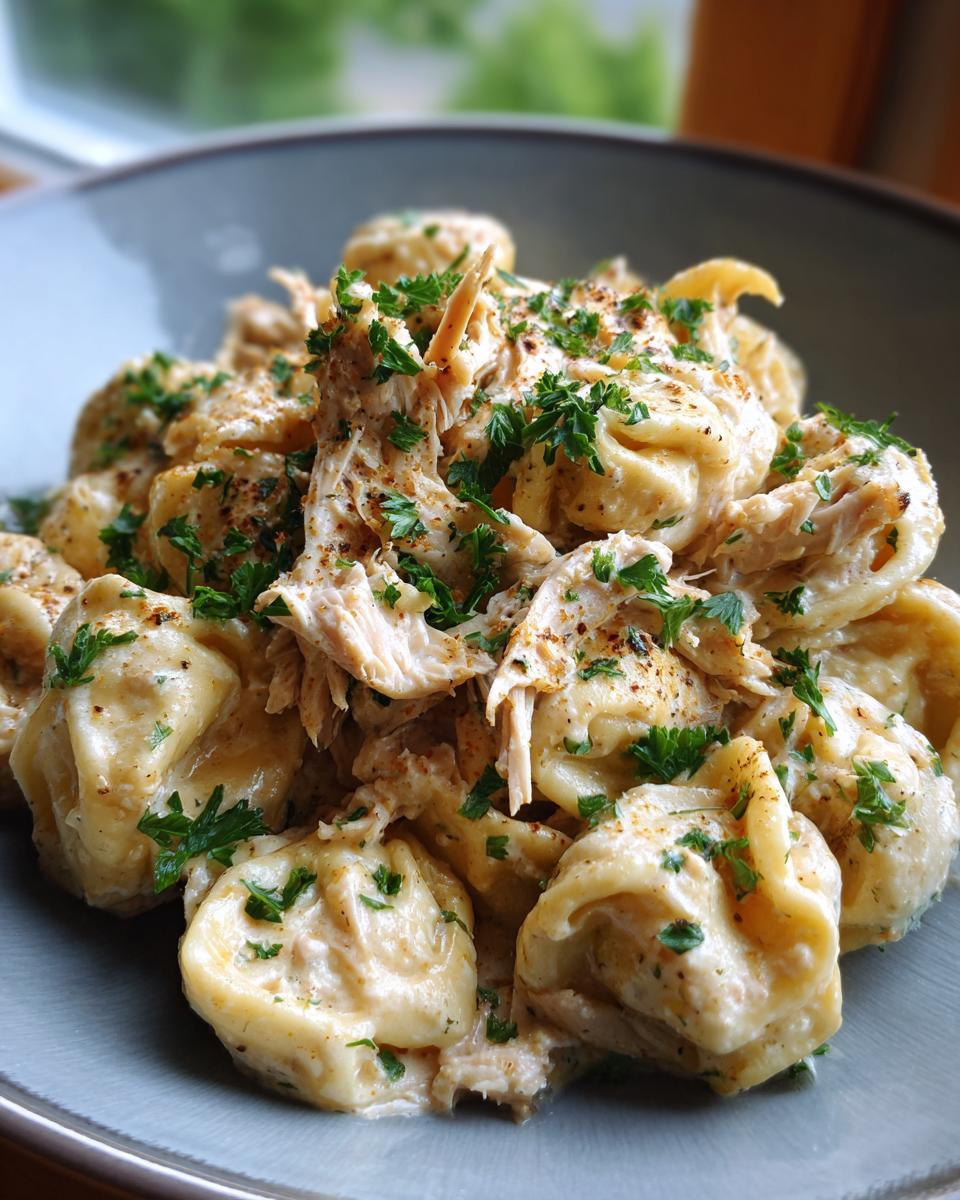 A close-up of a bowl filled with creamy crockpot chicken tortellini, garnished with fresh parsley.