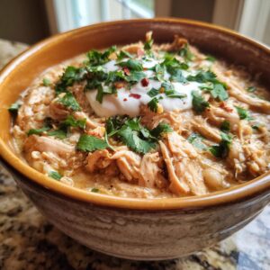 A close-up of a bowl of creamy crockpot white chicken chili topped with sour cream, cilantro, and red pepper flakes.