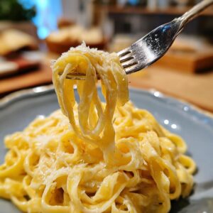 Close-up of a fork lifting creamy fettuccine alfredo pasta, sprinkled with parmesan cheese.