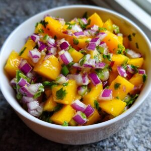 Close-up of a white bowl filled with vibrant mango salsa, featuring diced mango, red onion, and cilantro.