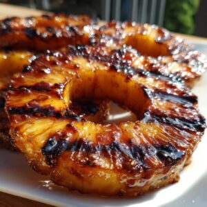 Close-up of juicy, caramelized grilled pineapple rings on a white plate, showcasing grill marks.