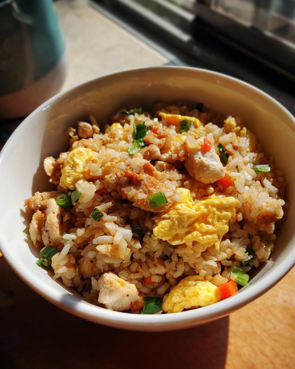 A close-up of a bowl filled with high protein chicken fried rice, featuring scrambled egg, chicken pieces, and green onions.