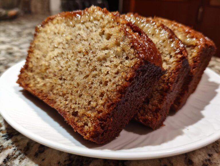 Three moist slices of honey vanilla banana bread on a white plate, showcasing a golden-brown crust and tender crumb.