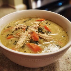 A close-up of a bowl of creamy keto chicken pot pie soup, featuring shredded chicken, carrots, and herbs.