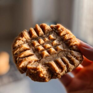 Close-up of a hand holding a classic peanut butter cookie with fork marks.