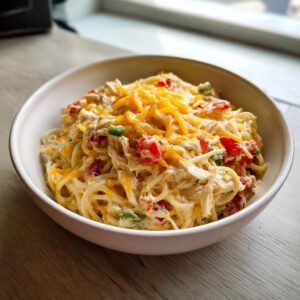 A bowl of creamy Rotel chicken spaghetti topped with melted cheddar cheese and diced tomatoes.
