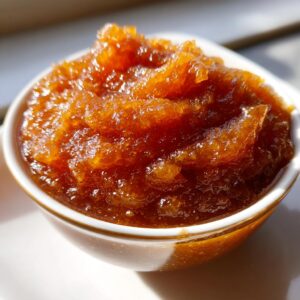 Close-up of rich, amber-colored pear butter in a white bowl, showcasing its smooth, spreadable texture.