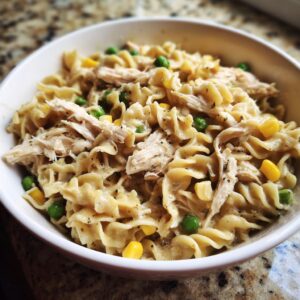 A bowl of slow cooker chicken pot pie pasta with shredded chicken, peas, and corn mixed with creamy sauce.