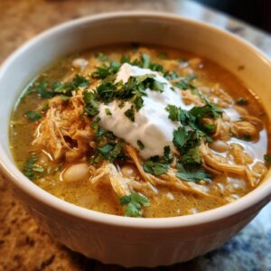 A close-up of a bowl filled with hearty slow cooker white chicken chili, topped with sour cream and fresh cilantro.