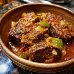 Close-up of tender smothered Swiss steak with green peppers and onions in a rich tomato-based sauce.