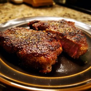 Two juicy steaks seasoned with a steak marinade, cooked to perfection and served on a dark plate.