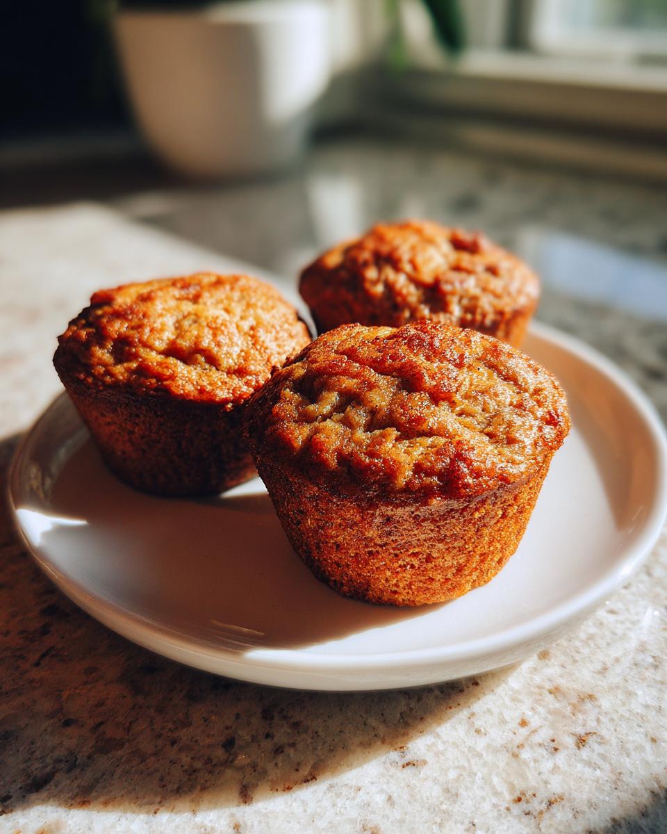 Three golden brown apple cinnamon Greek yogurt muffins on a white plate, bathed in sunlight.