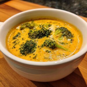 A close-up shot of a white bowl filled with creamy Broccoli Cheddar Soup, featuring tender broccoli florets.