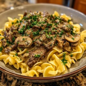 A close-up of a bowl of classic beef stroganoff, featuring tender beef slices, mushrooms, and a creamy sauce served over egg noodles, garnished with parsley.