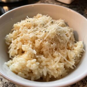 Close-up of a bowl filled with creamy parmesan rice, topped with shredded parmesan cheese and herbs.