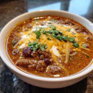 A close-up of a bowl of creamy taco soup, topped with shredded cheese, a dollop of sour cream, and fresh cilantro.