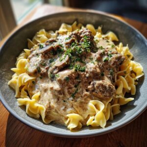 A close-up of a bowl of ground beef stroganoff served over egg noodles, garnished with fresh parsley.