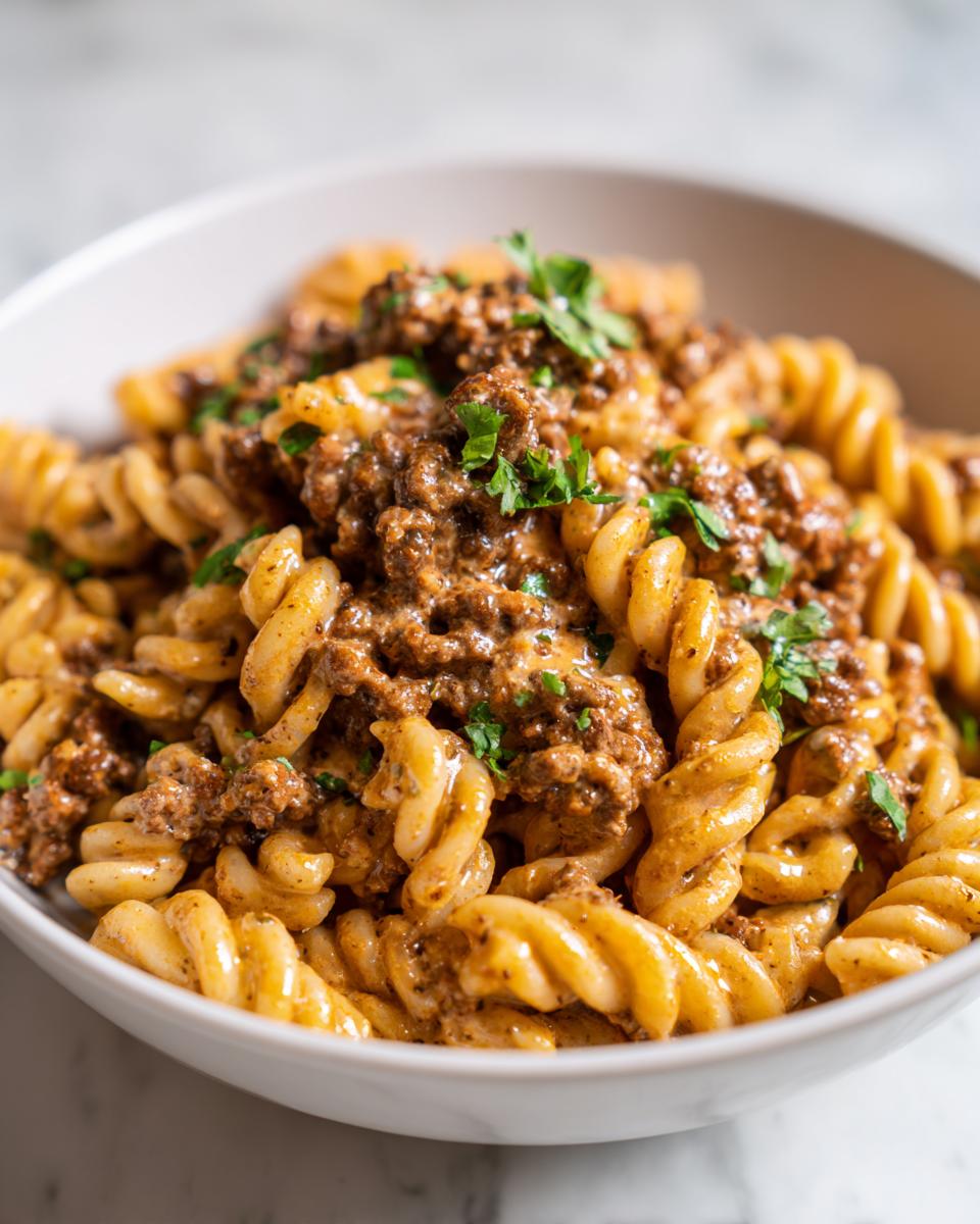 A bowl of high protein creamy beef pasta, featuring fusilli noodles coated in a rich sauce and topped with ground beef and fresh parsley.