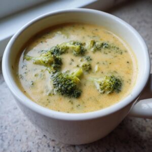 A creamy bowl of Panera broccoli cheddar soup with visible florets of broccoli.