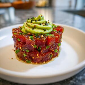 Close-up of a perfectly molded tuna tartare tower topped with piped avocado cream and sesame seeds.