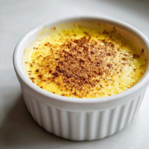 A creamy yellow egg custard topped with a sprinkle of caramelized sugar, served in a white fluted ramekin.